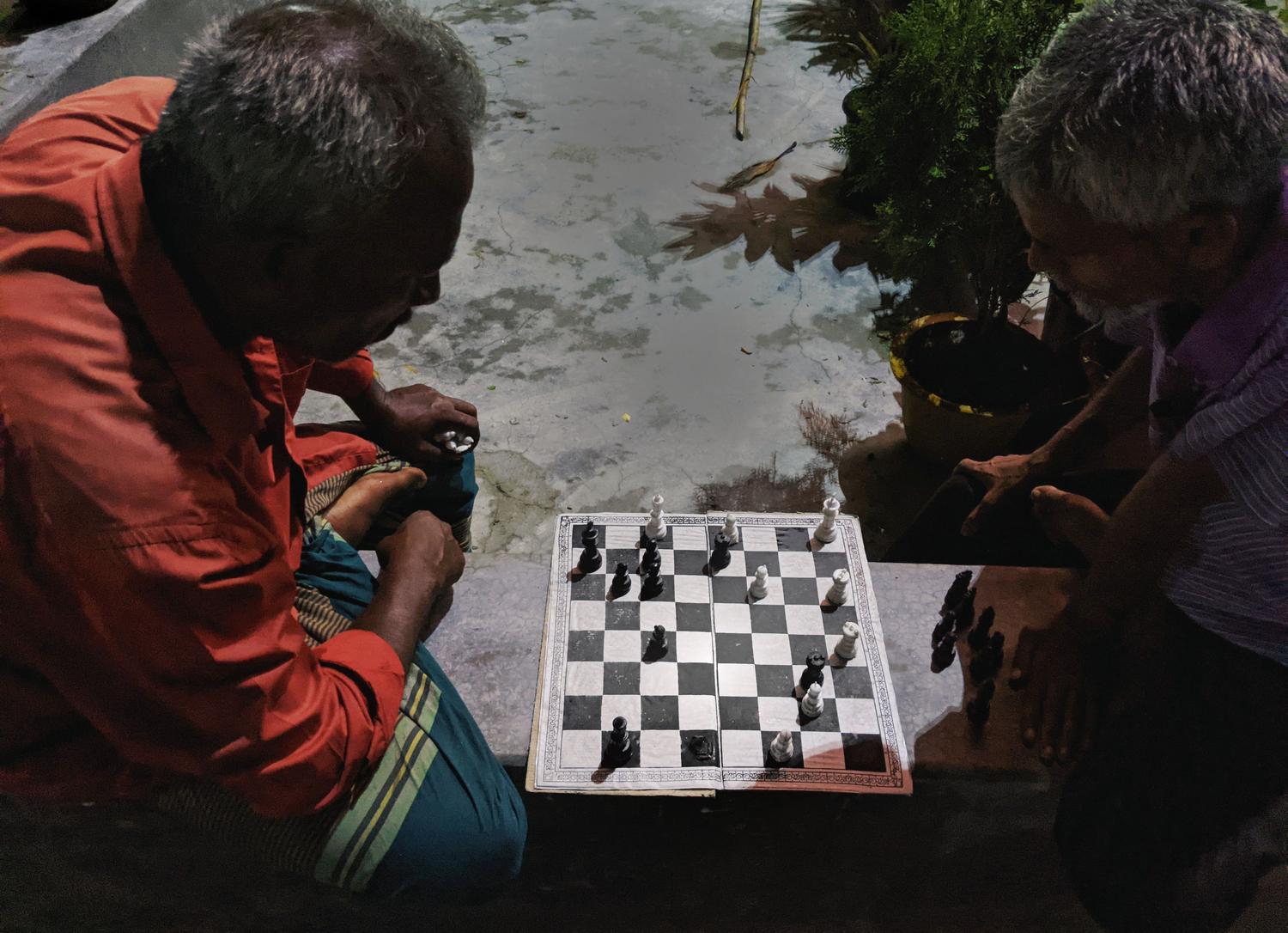 Dos hombres mayores concentrados en una partida de ajedrez al aire libre, representando el aspecto social y el ingenio del juego. Dos hombres mayores concentrados en una partida de ajedrez al aire libre, representando el aspecto social y el ingenio del juego.