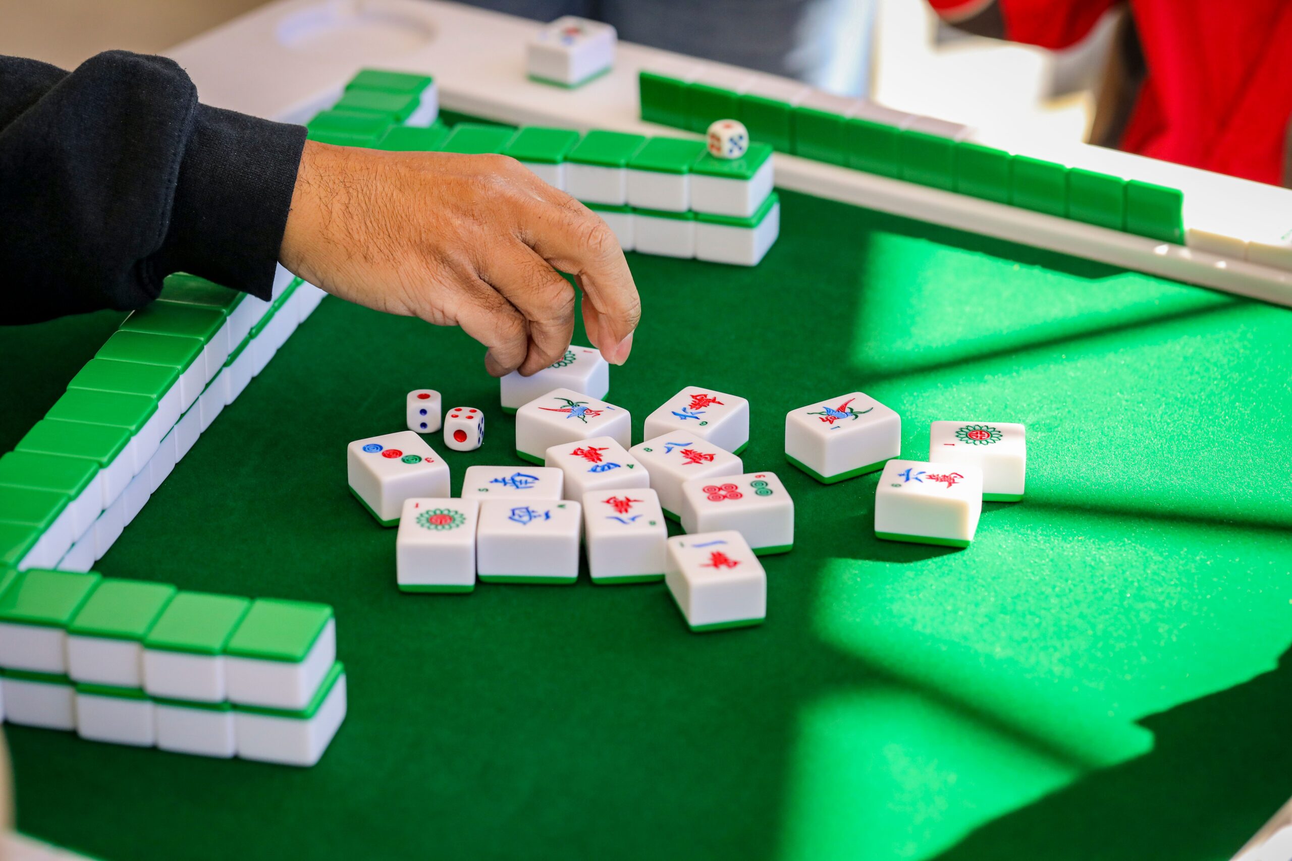 Mano de un jugador moviendo una ficha de Mahjong con precisión, representando la estrategia y concentración del juego. Mano de un jugador moviendo una ficha de Mahjong con precisión, representando la estrategia y concentración del juego.