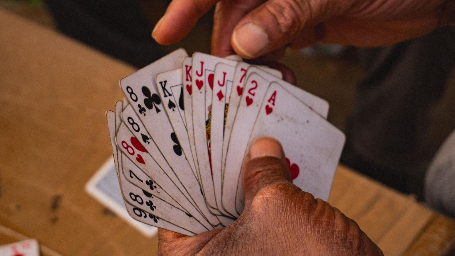 Manos de una persona mayor sosteniendo un abanico de cartas, representando la naturaleza intelectual y atemporal del juego de Bridge. Manos de una persona mayor sosteniendo un abanico de cartas, representando la naturaleza intelectual y atemporal del juego de Bridge.