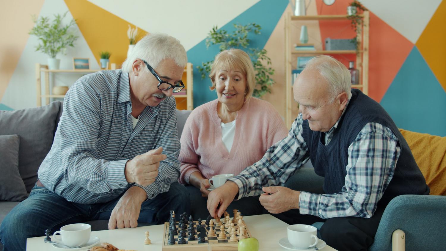 Ajedrez en adultos mayores Adultos mayores disfrutando de una partida de ajedrez en un ambiente acogedor para prevenir el deterioro cognitivo.