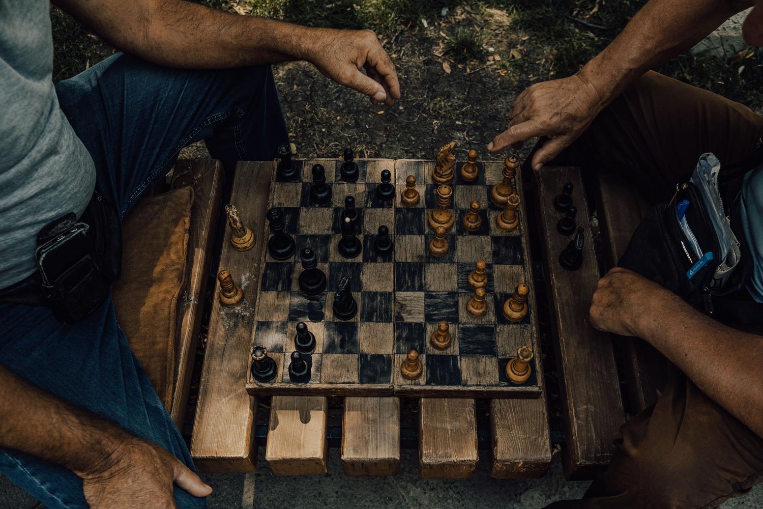Dos personas jugando al ajedrez en un entorno exterior casual, ilustrando la aplicación práctica de aperturas agresivas en el ajedrez amateur. Dos personas jugando al ajedrez en un entorno exterior casual, ilustrando la aplicación práctica de aperturas agresivas en el ajedrez amateur.