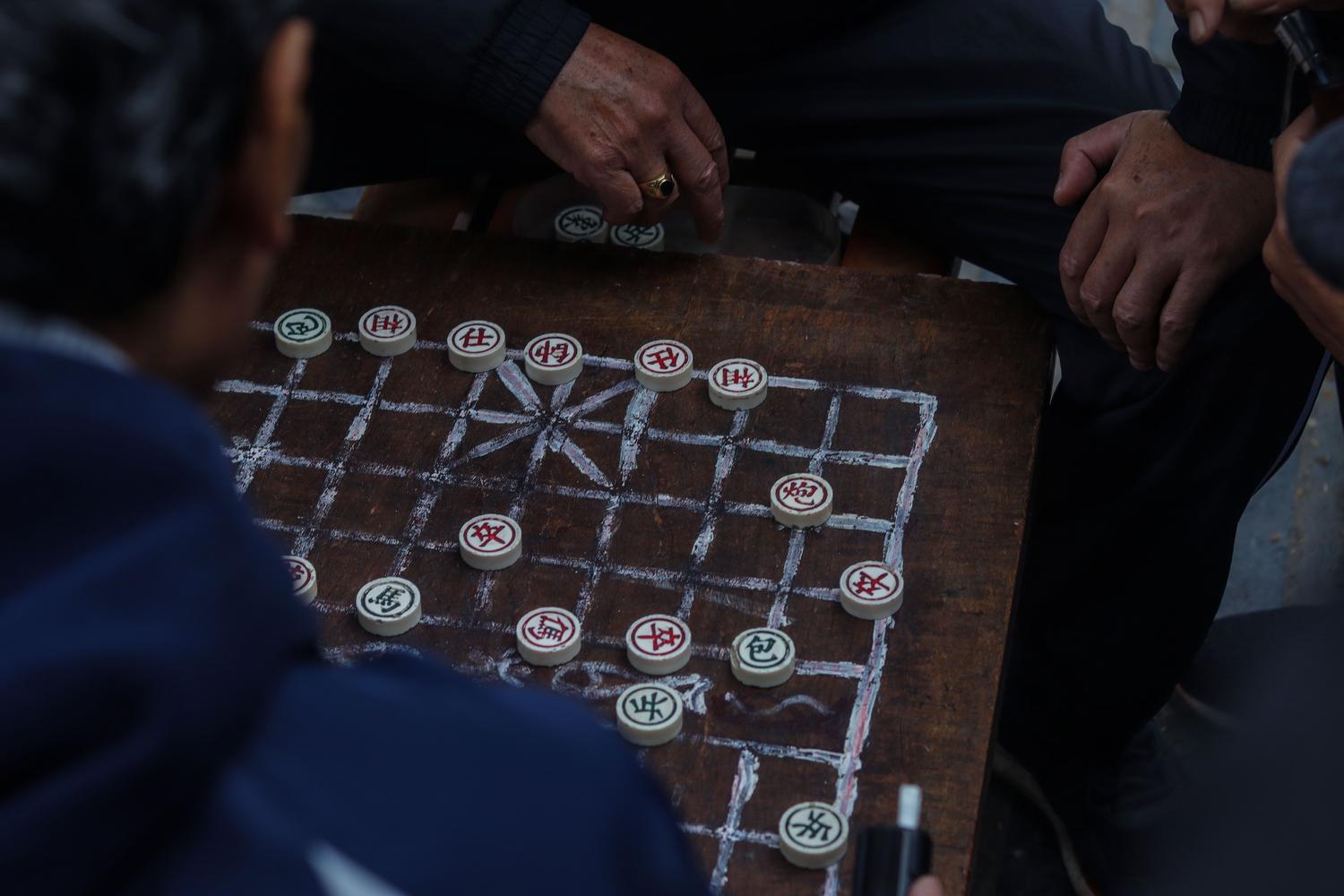 Jugadores concentrados en una partida de Xiangqi sobre un tablero rústico de madera. Jugadores concentrados en una partida de Xiangqi sobre un tablero rústico de madera.