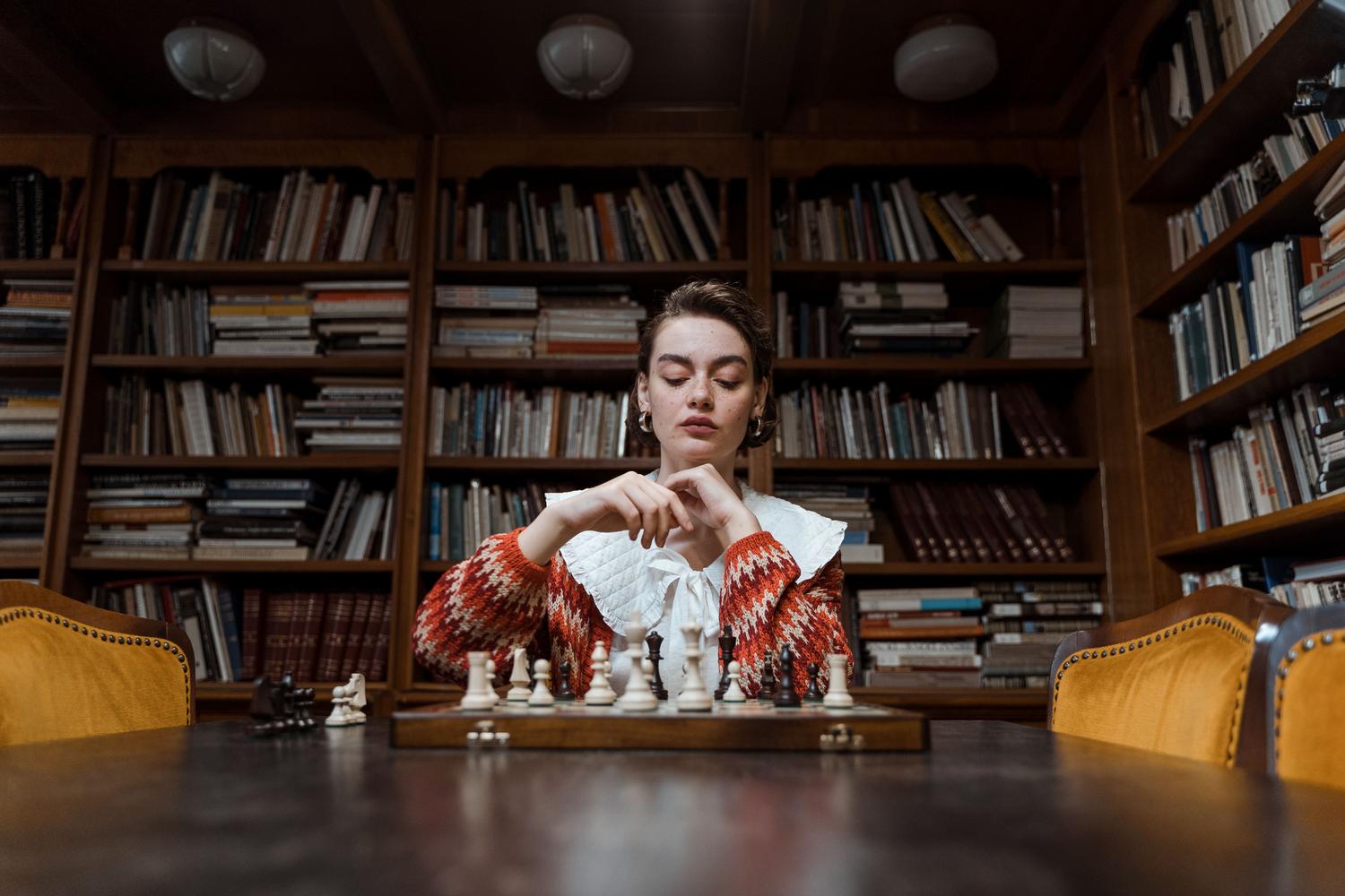 Mujer concentrada estudiando ajedrez en una biblioteca, simbolizando el estudio estructurado y la táctica. Mujer concentrada estudiando ajedrez en una biblioteca, simbolizando el estudio estructurado y la táctica.