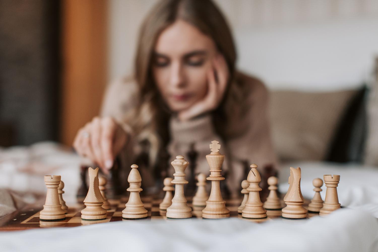 Mujer planificando su siguiente movimiento en una partida de ajedrez, destacando la concentración y el cálculo mental. Mujer planificando su siguiente movimiento en una partida de ajedrez, destacando la concentración y el cálculo mental.